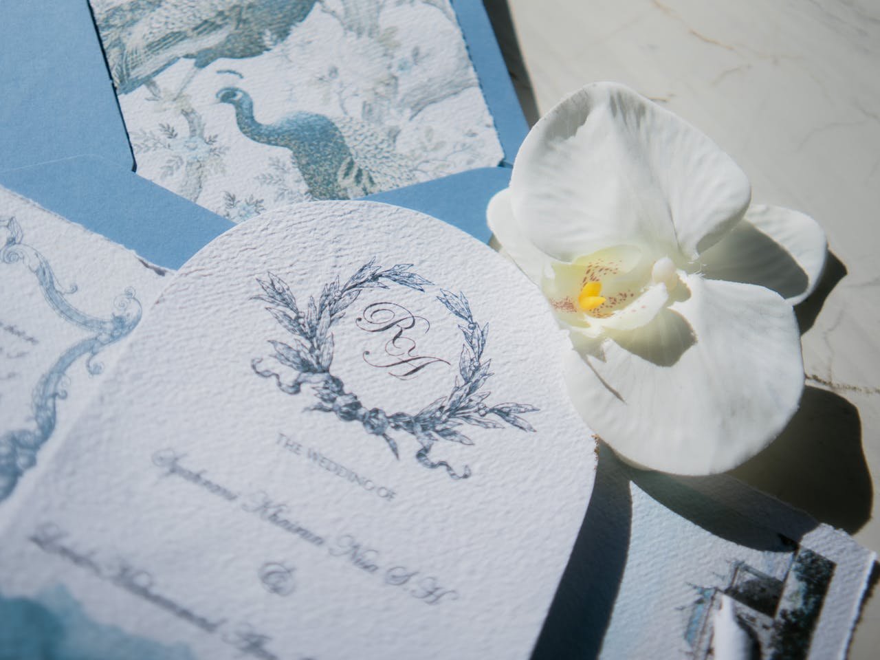 The Art of Drawing Readers In: Your attractive post title goes here A sophisticated wedding invitation set featuring blue tones and a white orchid embellishment.